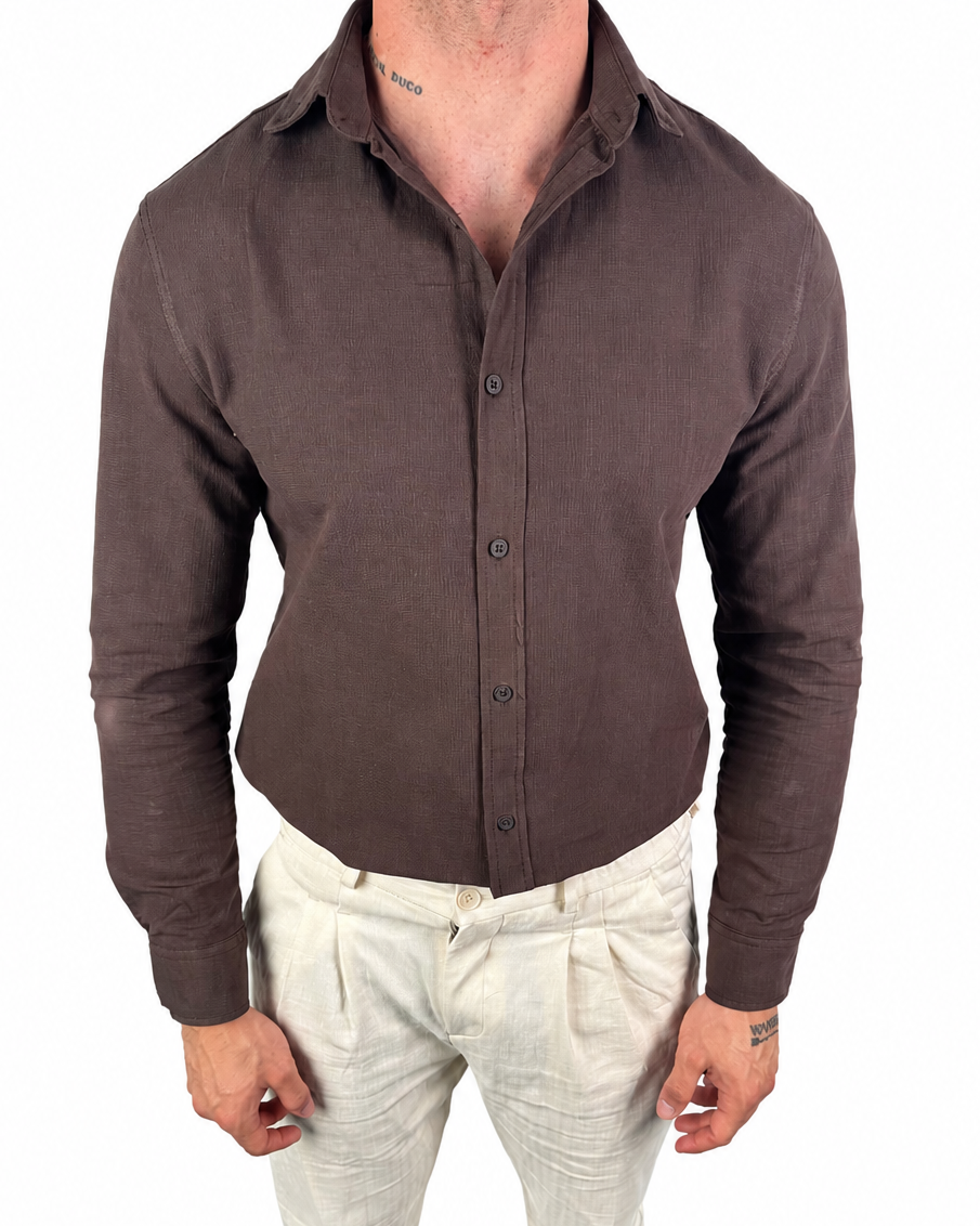 A man wearing a fitted, long-sleeve button-up shirt in dark brown and light beige linen trousers, shown from the neck down against a plain white background.