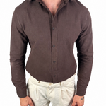 A man wearing a fitted, long-sleeve button-up shirt in dark brown and light beige linen trousers, shown from the neck down against a plain white background.