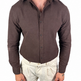 A man wearing a fitted, long-sleeve button-up shirt in dark brown and light beige linen trousers, shown from the neck down against a plain white background.