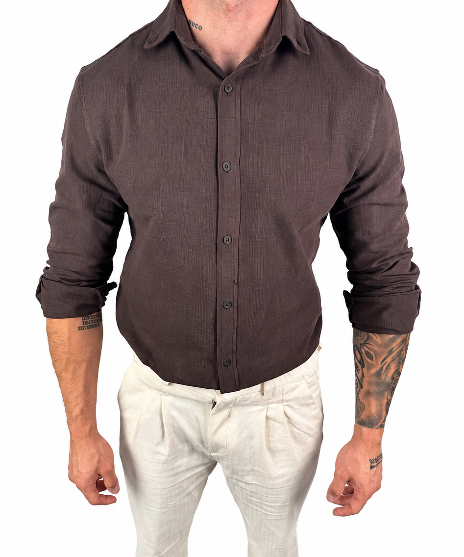 A man wearing a dark brown long-sleeve linen button-up shirt and off-white linen trousers, shown from the neck down against a plain white background.