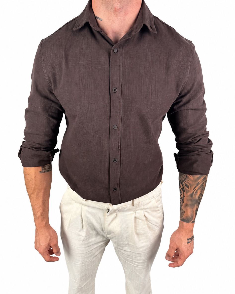 A man wearing a dark brown long-sleeve linen button-up shirt and off-white linen trousers, shown from the neck down against a plain white background.