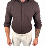 A man wearing a dark brown long-sleeve linen button-up shirt and off-white linen trousers, shown from the neck down against a plain white background.