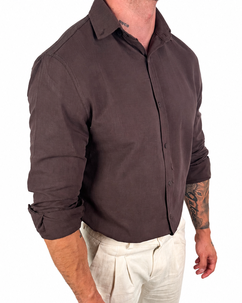 A man wearing a dark brown long-sleeve button-up shirt and off-white trousers, shown from the neck down against a plain white background.