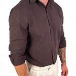 A man wearing a dark brown long-sleeve button-up shirt and off-white trousers, shown from the neck down against a plain white background.