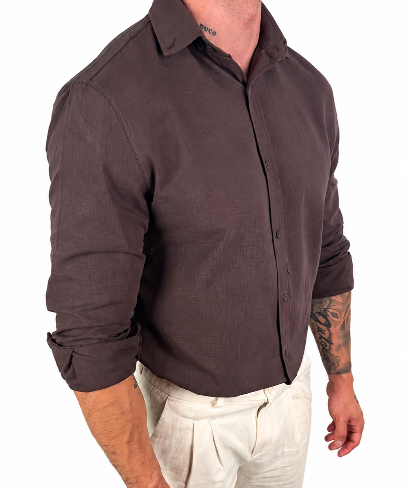 A man wearing a dark brown long-sleeve button-up shirt and off-white trousers, shown from the neck down against a plain white background.