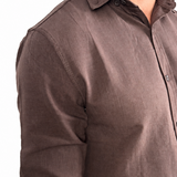 A man wearing a dark brown linen button-down shirt with rolled-up sleeves and off-white trousers, shown from the chest down against a white background.