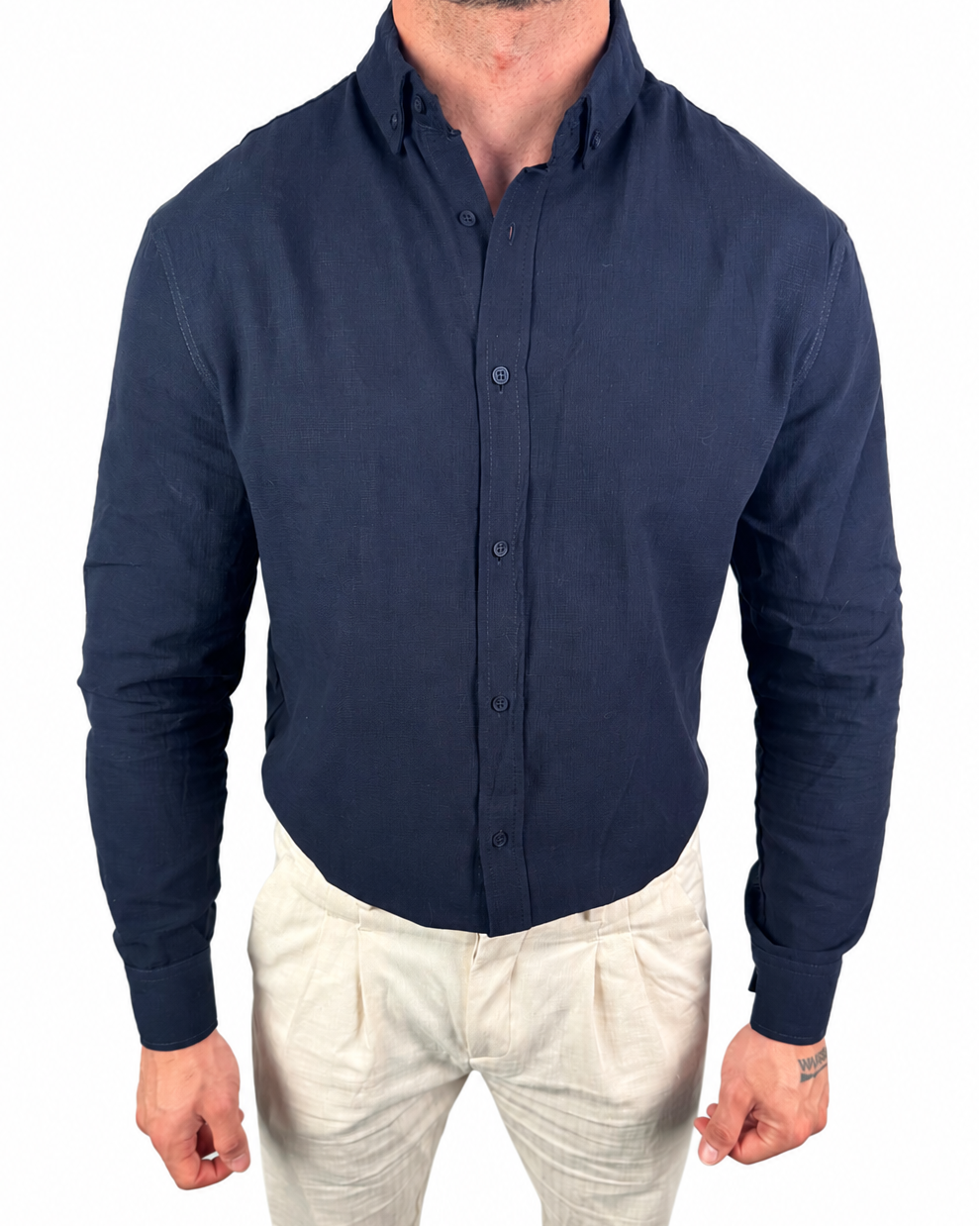 A man wearing a dark navy blue long-sleeve button-down shirt and light beige trousers, shown from the neck down against a plain white background.