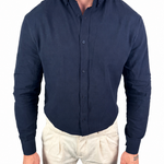 A man wearing a dark navy blue long-sleeve button-down shirt and light beige trousers, shown from the neck down against a plain white background.