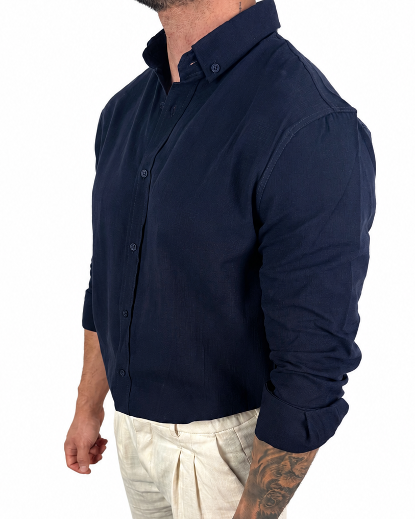A man wearing a dark navy long-sleeve button-down shirt and light beige trousers, shown from the side against a plain white background.