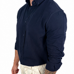 A man wearing a dark navy long-sleeve button-down shirt and light beige trousers, shown from the side against a plain white background.