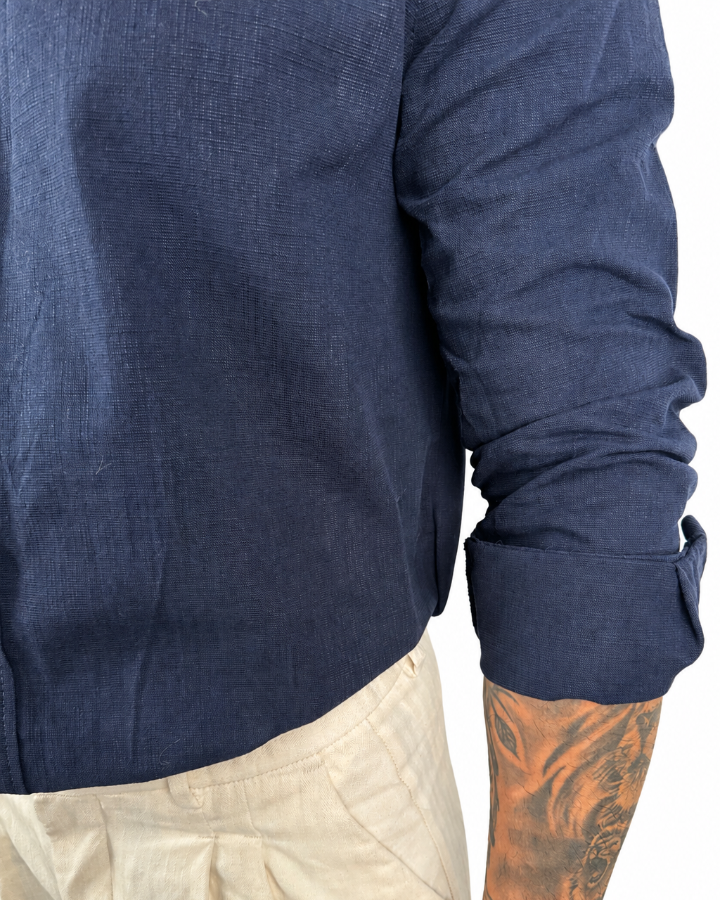 Close-up of a person wearing a navy blue long-sleeve linen shirt with rolled cuffs, paired with light beige trousers, against a white background.