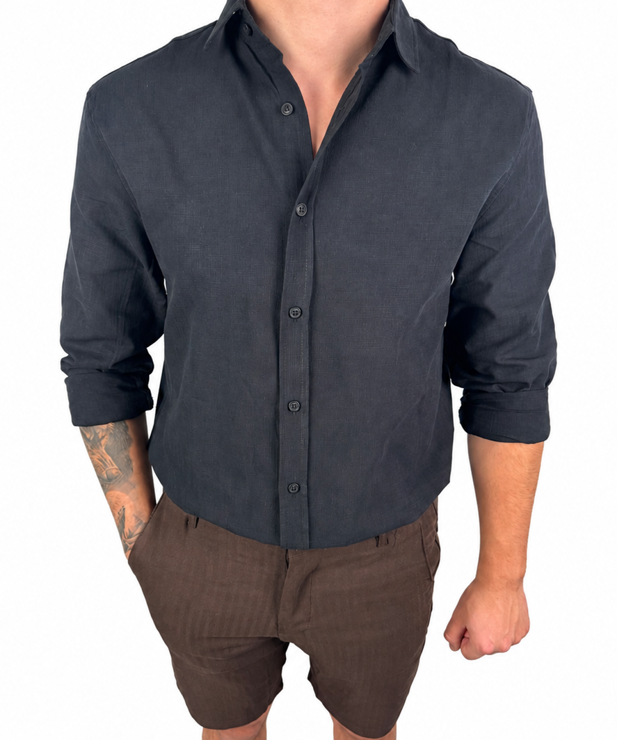A man wearing a dark charcoal gray long-sleeve linen button-down shirt and brown pinstriped linen shorts, standing against a solid white background.