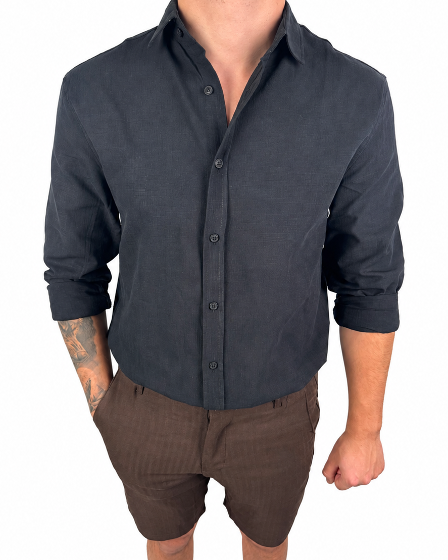 A man wearing a dark charcoal gray long-sleeve linen button-down shirt and brown pinstriped linen shorts, standing against a solid white background.