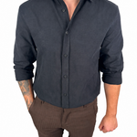A man wearing a dark charcoal gray long-sleeve linen button-down shirt and brown pinstriped linen shorts, standing against a solid white background.