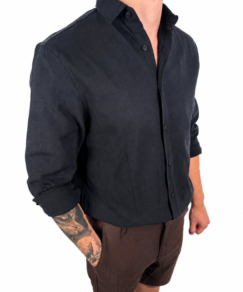 A man wearing a black long-sleeve linen button-up shirt and brown linen shorts, shown from the neck down against a white background.