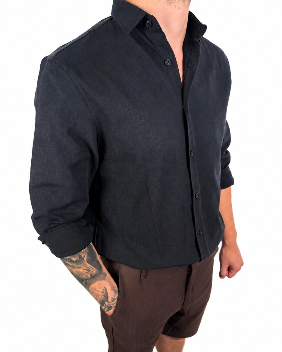 A man wearing a black long-sleeve linen button-up shirt and brown linen shorts, shown from the neck down against a white background.