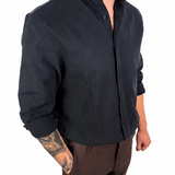 A man wearing a black long-sleeve linen button-up shirt and brown linen shorts, shown from the neck down against a white background.