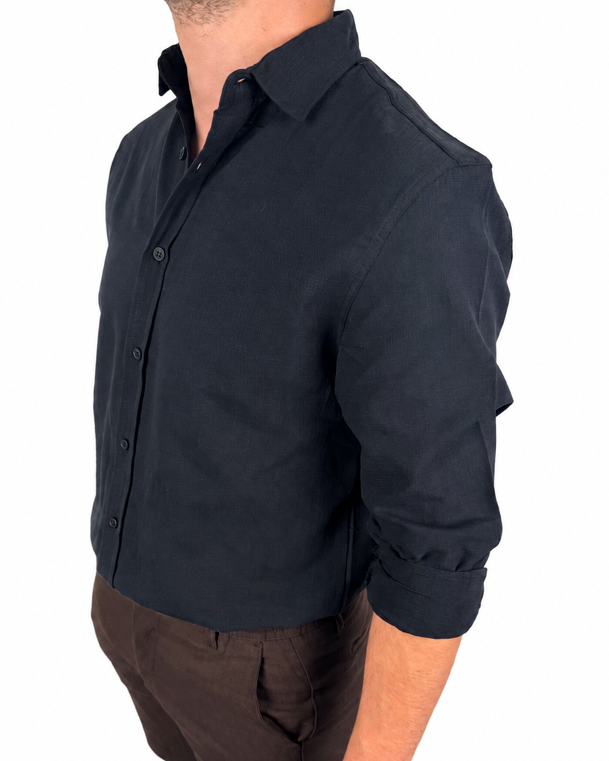 A man wearing a dark navy long-sleeve button-up shirt with rolled-up sleeves, paired with brown shorts and black socks, shown from a side profile against a white background.