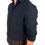 A man wearing a dark navy long-sleeve button-up shirt with rolled-up sleeves, paired with brown shorts and black socks, shown from a side profile against a white background.