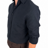 A man wearing a dark navy long-sleeve button-up shirt with rolled-up sleeves, paired with brown shorts and black socks, shown from a side profile against a white background.