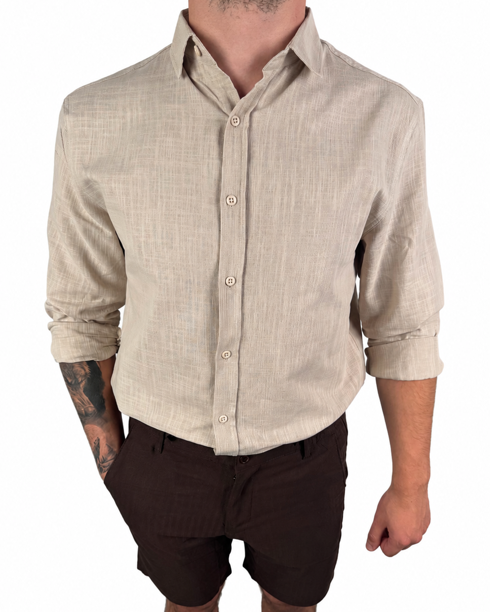 A man wearing a light beige linen long-sleeve button-down shirt and dark brown shorts, shown from the neck down against a plain white background.