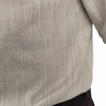 Close-up of a man wearing a light beige linen shirt with rolled-up sleeves and dark trousers, against a plain white background.