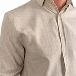 A man wearing a light beige linen button-down shirt with rolled-up sleeves and dark brown trousers, shown from the chest down against a white background.
