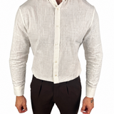 A man wearing a light beige textured linen button-down shirt and dark brown trousers, shown from the neck down against a plain white background.