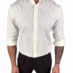 A man wearing a light beige linen long-sleeve button-down shirt with rolled-up sleeves and black trousers, shown from the neck down against a plain white background.