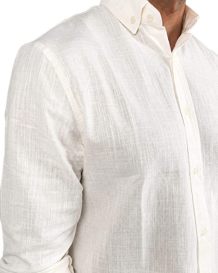 A close-up of a man wearing a textured off-white linen button-down shirt with rolled-up sleeves, paired with dark trousers.