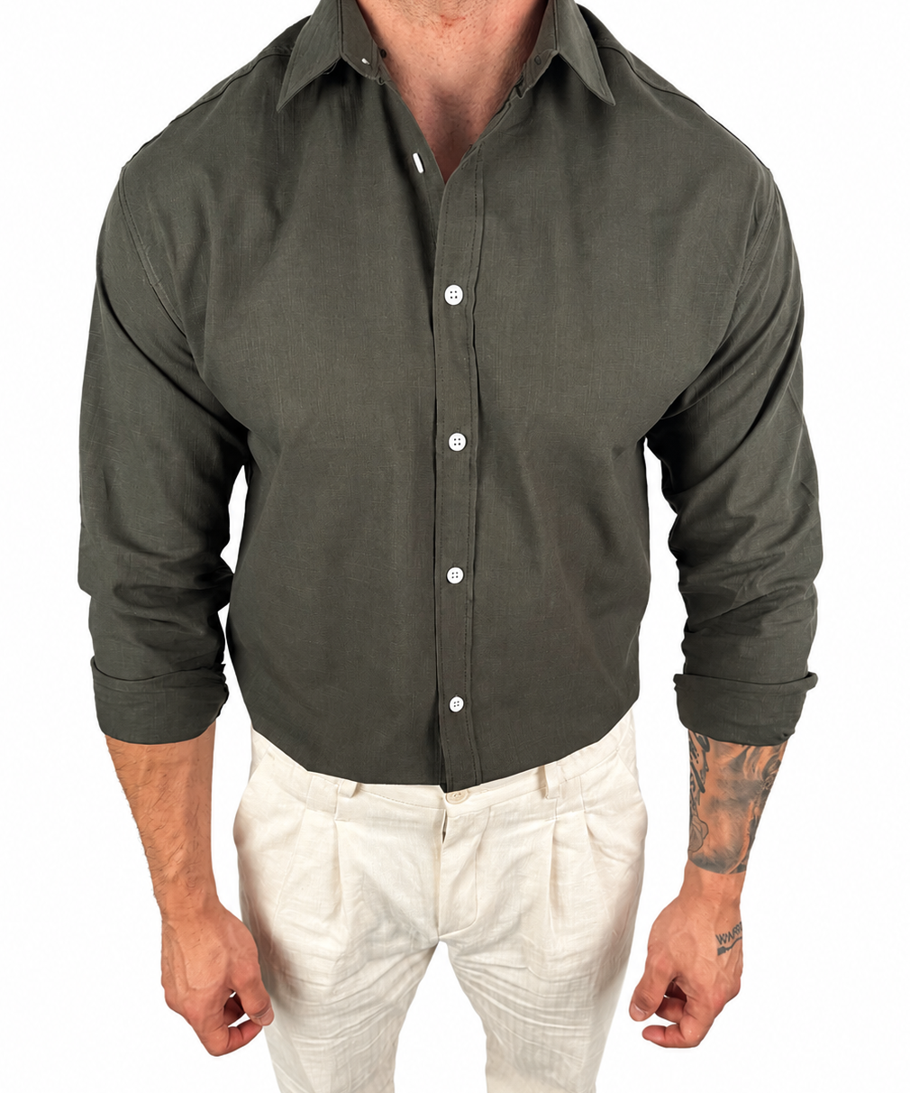 A man wearing a dark olive green long-sleeve button-down shirt and off-white trousers, shown from the neck down against a plain white background.