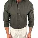 A man wearing a dark olive green long-sleeve button-down shirt and off-white trousers, shown from the neck down against a plain white background.