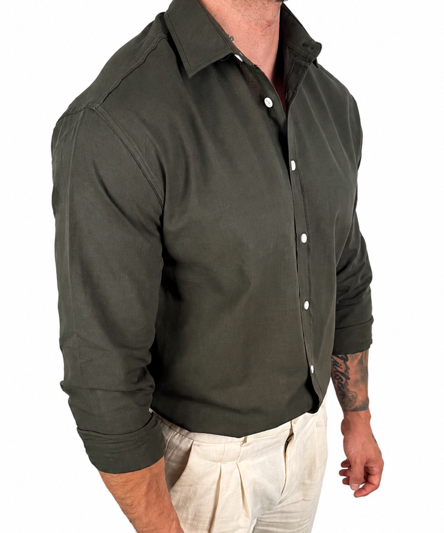 A man wearing a dark olive green long-sleeve button-down shirt and light beige trousers, shown from the neck down against a plain white background.