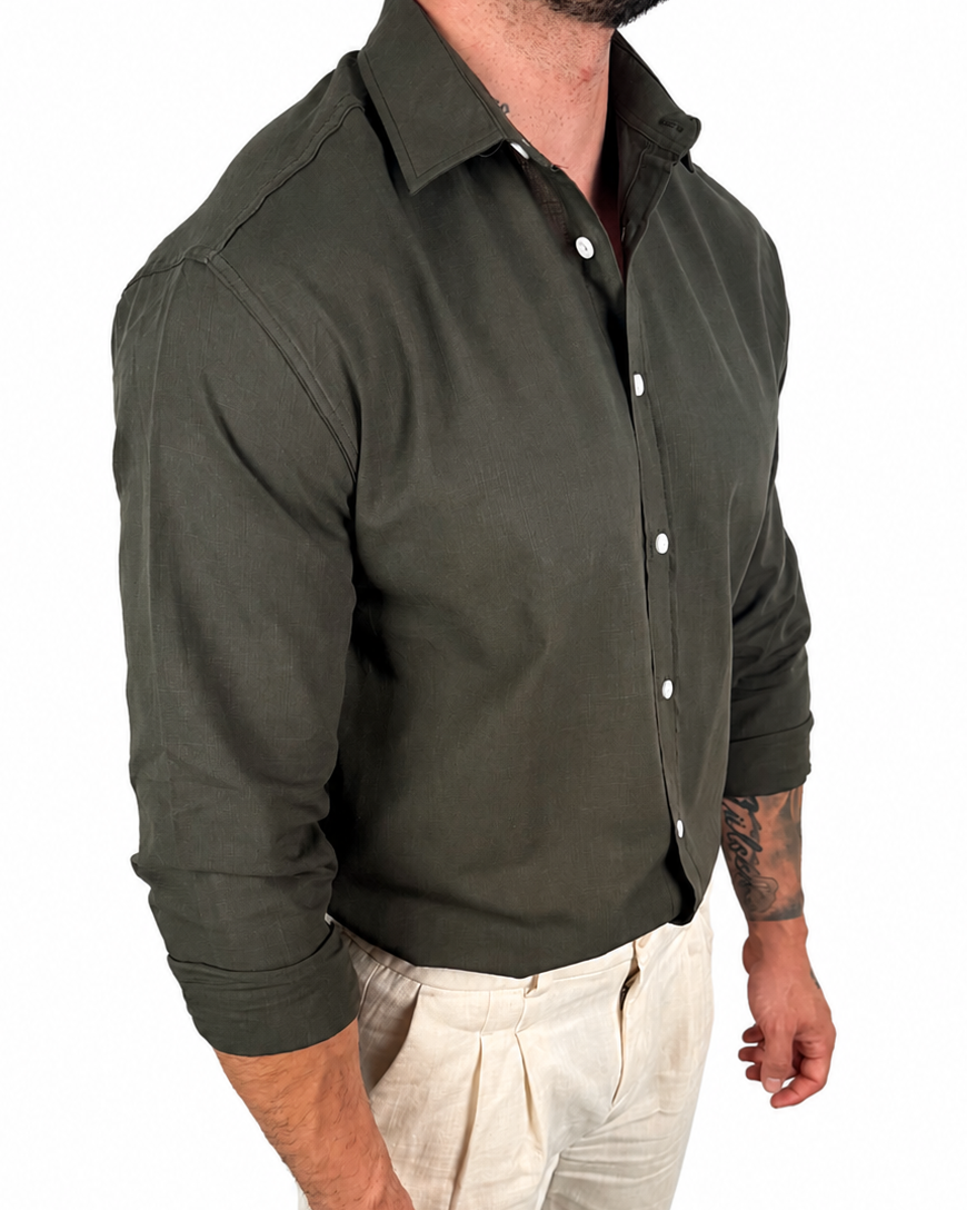 A man wearing a dark olive green long-sleeve button-down shirt and light beige trousers, shown from the neck down against a plain white background.