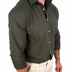 A man wearing a dark olive green long-sleeve button-down shirt and light beige trousers, shown from the neck down against a plain white background.