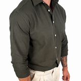 A man wearing a dark olive green long-sleeve button-down shirt and light beige trousers, shown from the neck down against a plain white background.