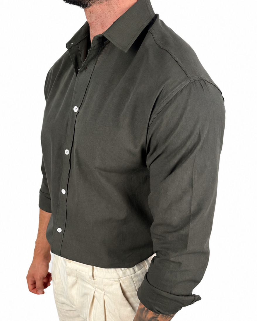 A man wearing a dark olive green long-sleeve button-down shirt and light beige trousers, shown from a side profile against a plain white background.