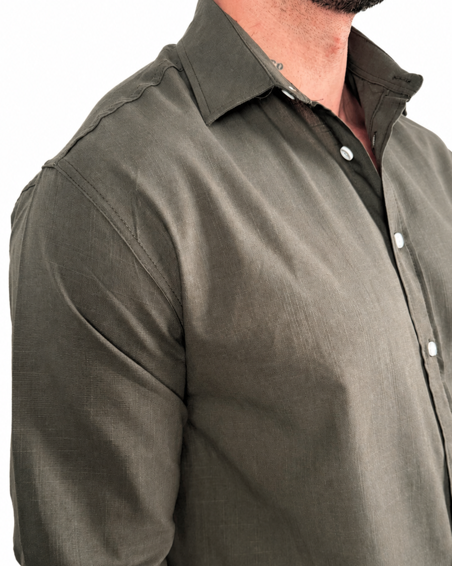 A man wearing a dark olive green long-sleeve linen button-down shirt, paired with light beige pants, shown from the chest down against a white background.