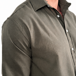 A man wearing a dark olive green long-sleeve linen button-down shirt, paired with light beige pants, shown from the chest down against a white background.