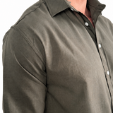 A man wearing a dark olive green long-sleeve linen button-down shirt, paired with light beige pants, shown from the chest down against a white background.