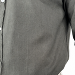 Close-up of a dark gray linen button-up shirt with a visible linen weave texture, worn by a model with light beige pants visible at the bottom.