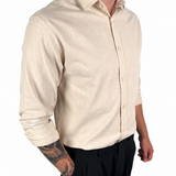 A man wearing a light beige linen button-down shirt and black trousers, shown from the neck down against a plain white background.