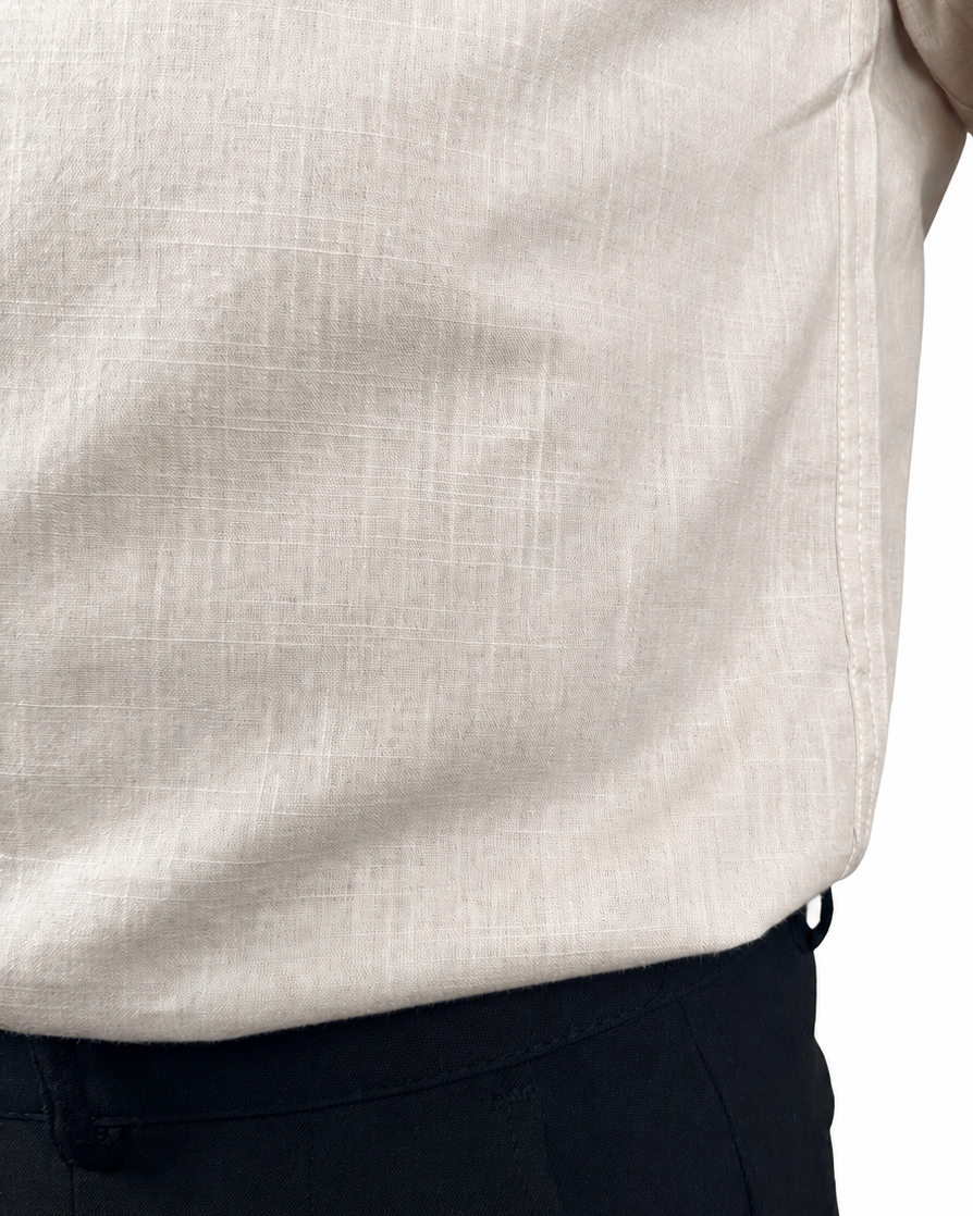 Close-up of a person wearing a light beige linen shirt tucked into dark trousers, showing the fabric texture and waistband.