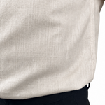 Close-up of a person wearing a light beige linen shirt tucked into dark trousers, showing the fabric texture and waistband.