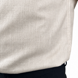 Close-up of a person wearing a light beige linen shirt tucked into dark trousers, showing the fabric texture and waistband.