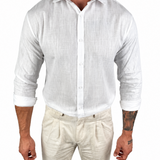 A man wearing a white long-sleeve linen button-up shirt and light beige linen trousers, shown from the neck down against a plain white background.