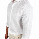 A man wearing a white long-sleeve linen button-down shirt and beige trousers, shown from the side against a plain white background.