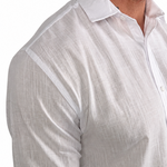 A close-up of a man wearing a white long-sleeve linen button-down shirt, showing the textured fabric and collar against a plain white background.