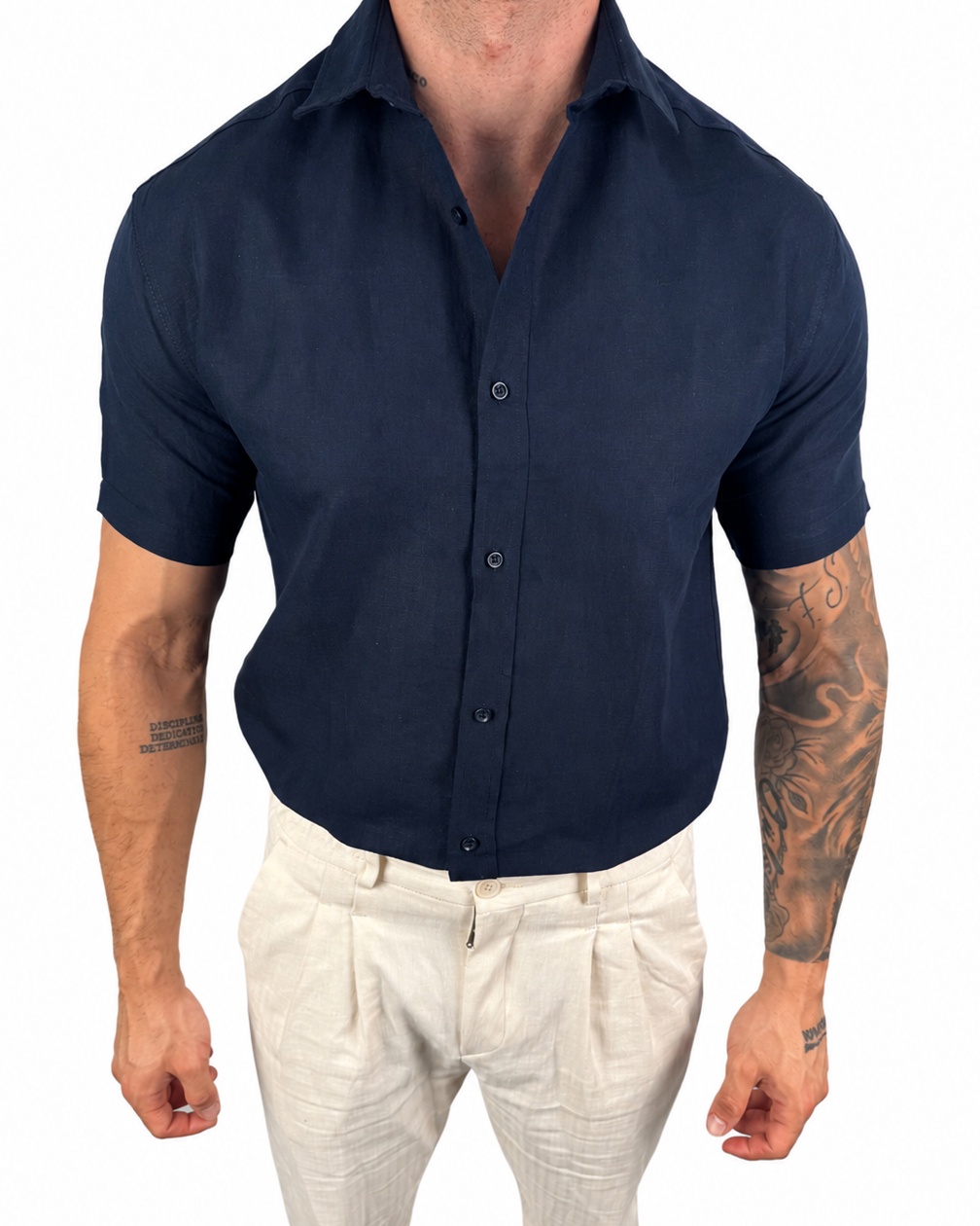 A man wearing a dark navy blue short-sleeve button-down shirt tucked into off-white trousers, shown from the neck down against a plain white background.