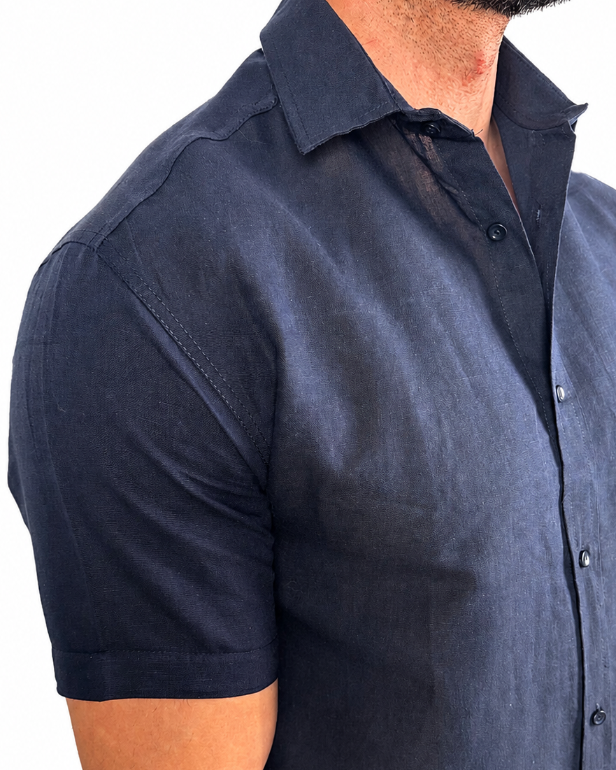 A man wearing a dark navy blue short-sleeve linen button-down shirt, shown from the chest down against a plain white background.